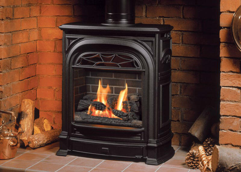 Valor Portrait Stove set in existing  brick fireplace hearth with logs and kettle to the left