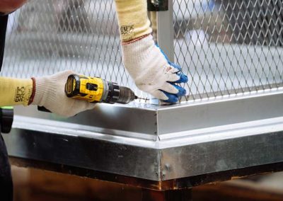 Close up of technician's gloved hands fabricating screen on stainless steel chimney cap