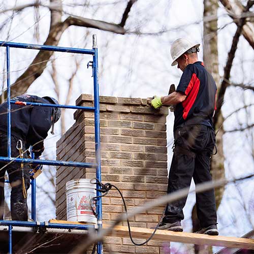 Two Technicians Completing Brick Chimney Restoration on Roof