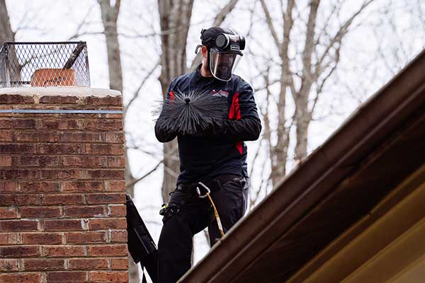 Chimney technician standing on roof holding sweep broom near chimney