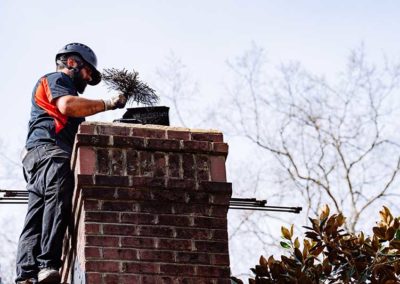 Technician standing next to chimney completing chimney sweep with brush