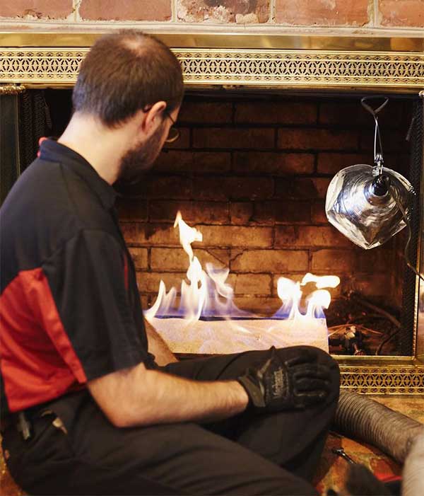 Chimney technician inspecting lit fireplace logs in fireplace