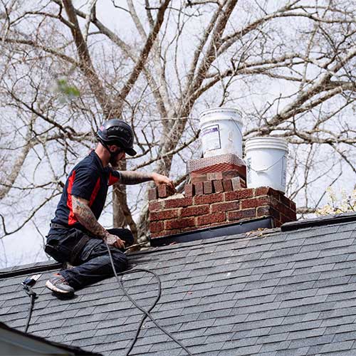 Chimney technician repairing cracked mortar around chimney cap