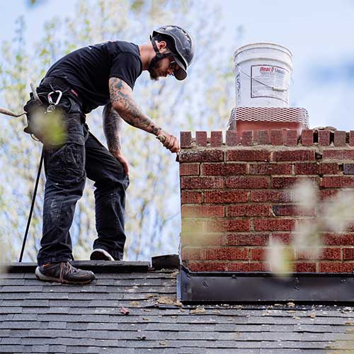 Close up view of chimney technician on roof repairing mortar on chimney
