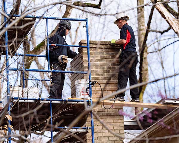 Two chimney technicians on a roof with scaffolding restoring brick chimney
