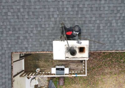 Aerial view of technician using sweep brush in chimney flue
