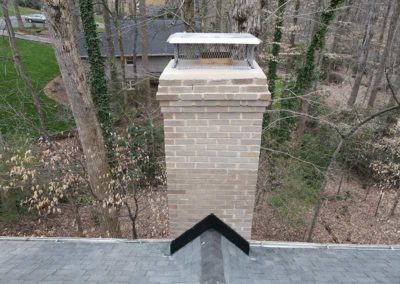 Completed repair and restoration of beige brick chimney with new cap and screen