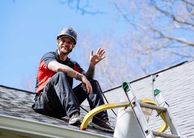 Technician sitting on roof near ladder smiling waiving