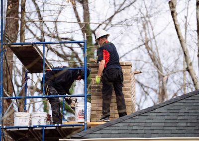 Two chimney technicians on a roof with scaffolding restoring brick chimney