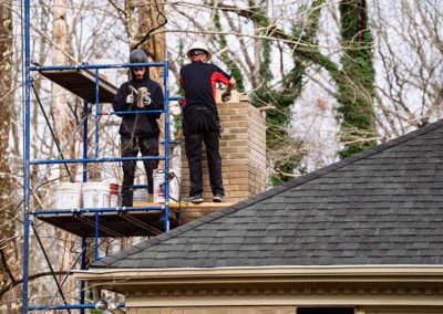 Zoomed out view of two technicians on roof repairing brick and mortar on chimney