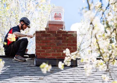 Side view of technician on roof laying mortar around chimney