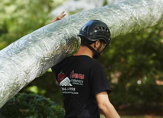 Chimney technician carrying brand new stainless steel chimney liner on shoulder
