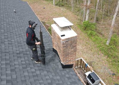 Technician cleaning and packing up on roof after completing new chimney cap install