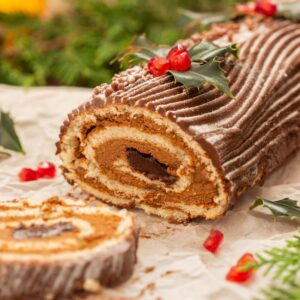 a yule log cake with holly and berries surrounding it