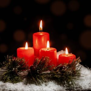 four red candles lit around a green wreath with fake snow surrounding