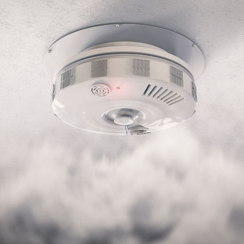 smoke traveling up to a white smoke detector on a ceiling